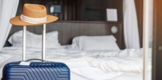 Blue luggage bag with hat on handle next to hotel room bed